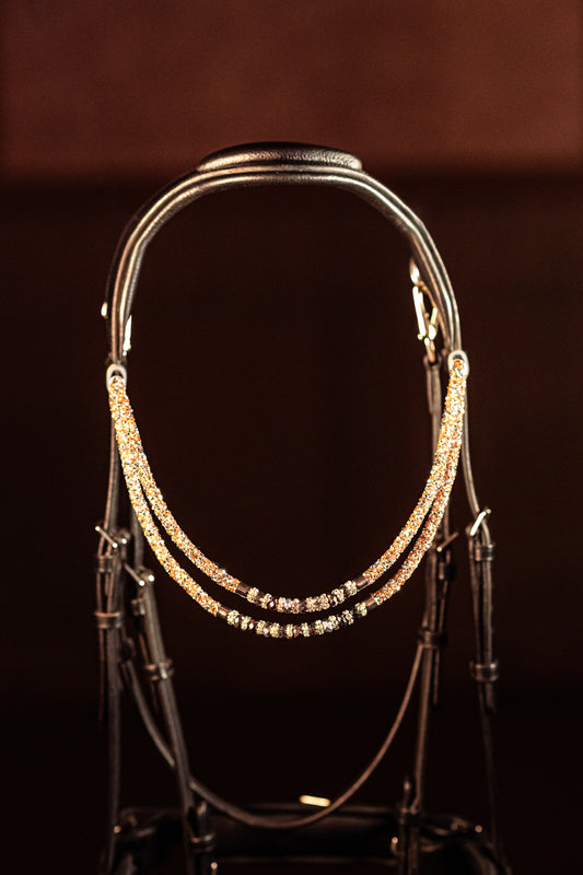 Horse browband Spectrum Double Topaz with beads browband by IBV Equine
Experience a new dimension of browband design. Crafted with a pair of soft,
flexible tubes, each generously sprinkled with dazzling rhinestones, this piece offers a unique texture and radiant sparkle. An internal metal wire allows for effortless shaping, ensuring a perfect contour to your horse's brow and maintaining its elegant form.
Each browband is handmade from scratch using premium European materials and durable leather. Featu