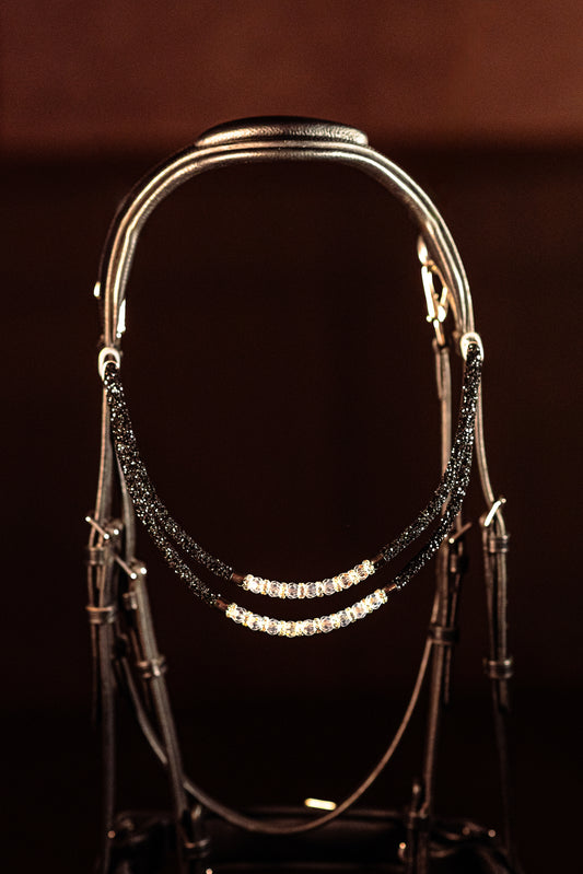 Horse browband Spectrum Double Black with beads browband  by IBV Equine
Experience a new dimension of browband design. Crafted with a pair of soft,
flexible tubes, each generously sprinkled with dazzling rhinestones, this piece offers a unique texture and radiant sparkle. An internal metal wire allows for effortless shaping, ensuring a perfect contour to your horse's brow and maintaining its elegant form.
Each browband is handmade from scratch using premium European materials and&nbsp;durable leather. Featu